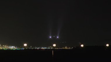 Gece yarısı havaalanı ışıklarıyla çevrili, farları yanan uçaklar piste yaklaşıyor..
