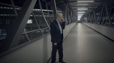 Fütüristik bir ortamda, ciddi davranışları olan bir iş adamı yüksek bir yürüyüş yolunda yürüyor, cep telefonuyla konuşuyor.