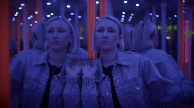 Genç bir kadın ayna labirentinin içinde parlak fütüristik bir ortamda yansımaları ve ışıkları var.