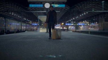 Geceleri, yalnız bir yolcu, bir bavulla ıssız bir tren istasyonunda yalnızlık ve gizem havasını yakalıyor.