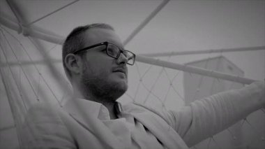 Modern mimari ortamda poz veren gözlüklü bir işadamı, siyah-beyaz bir şekilde yakalandı.