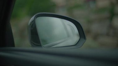 Aracın yan aynasının detaylı görüntüsü bulanık bir arkaplanda yağmur damlalarıyla kaplıdır.