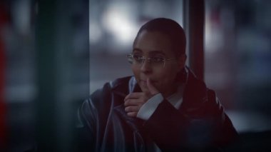 Yakın plan çekimde, gözlüklü genç bir adam arka planda bir şehir manzarası ile gece konuşur.