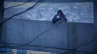 Loş bir kentsel çevrede beton bir yapının üzerinde el feneri olan gizemli kapüşonlu kişi..