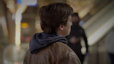 Genç bir adam, bulanık arka planda şehir ışıklarıyla, gece şehir ortamında duruyor, dalgın dalgın bakıyor.