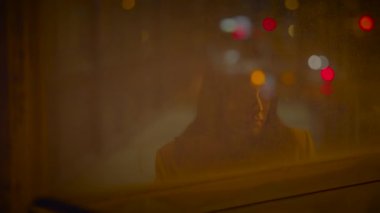 Gizemli figür bulanık gece hayatı ve şehir ışıklarına karşı gölgelenmiş, rüya gibi bir atmosfer yaratıyor..