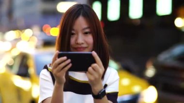 Trafiği ve arka planda ışıkları olan hareketli bir caddede genç bir kadın akıllı telefon kullanıyor.