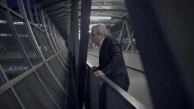 Geceleri cam koridorda iş adamı, iş kararlarını ve geleceği düşünüyor, ciddiyet ve yorgunluk gösteriyor.
