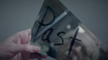 Bir insan kırık bir ayna parçası tutuyor ve üzerinde 