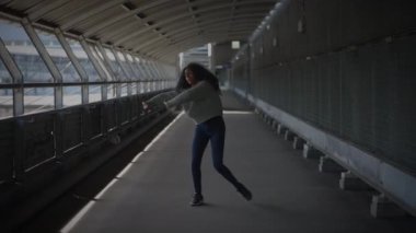 Kendine güvenen bir kadın, cam pencereleri ve metal iskeleti olan modern bir yaya köprüsünde güven içinde poz veriyor.