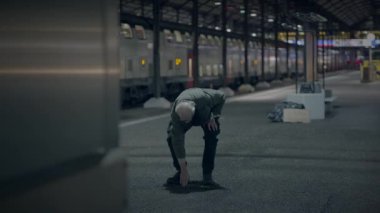 Tren istasyonunda, yaşlı bir adam düşüncelere dalmış, sakin bir akşamda bir siluet çiziyor.