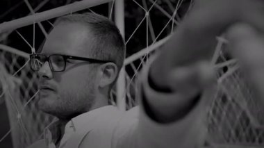 Gözlüklü ve beyaz gömlekli şık bir adam geometrik kabloya karşı poz veriyor, çağdaş görünüş sergiliyor.