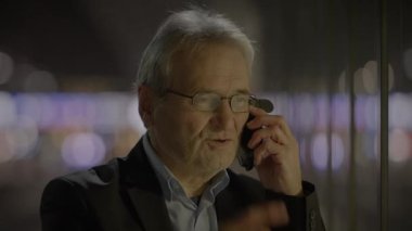 Kıdemli işadamı, arka planda bulanık şehir ışıklarıyla geceleyin önemli bir telefon görüşmesi yapıyor..