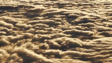 Çarpıcı bir hava manzarası, gökyüzünde dönen altın günbatımı bulutlarının güzelliğini yakalar, dalgalar denizini andırır.