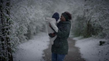 Anne ve çocuk, karlı bir ormanda huzurlu bir kış gününde birlikte doğanın güzelliğinin tadını çıkarıyorlar.