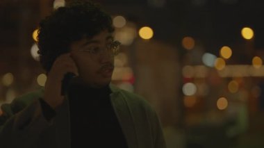 Gecenin karanlığında, gözlüklü ve ceketli şık bir adam şehir ışıklarının arasında bir telefon görüşmesi yapıyor.