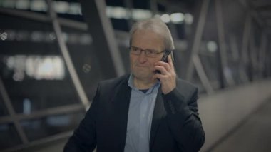 Geceleri modern bir şirket binasında, orta yaşlı bir işadamı akıllı telefonuyla bir telefon görüşmesi yapıyor.