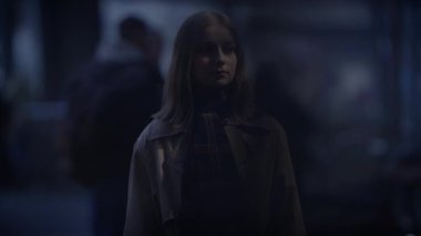 Genç bir kadın alacakaranlıkta şehir sokağında yalnız, bulanık insanlarla çevrili, sakin, zarif ve huzurlu bir hava yayıyor.