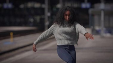 Yeşil kazaklı şık bir genç kadın, arka planı bulanık bir tren istasyonunda sakince bekliyor.