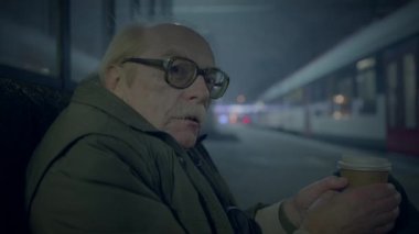 Yaşlı bir adam, gece boyunca tren istasyonunda elinde bir kahve fincanı, dalgın dalgın dalgın dalgın dalgın dalgın dalgın oturuyor.
