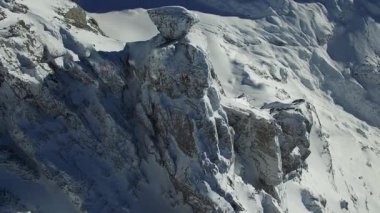 Karla kaplı bir dağ zirvesi göz kamaştırıcı güneş ışığında duruyor, engebeli arazinin ortasında büyüleyici bir manzara sağlıyor.