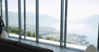 Zemin tavan pencereli modern oturma odası çarpıcı bir dağ ve göl manzarası sunarak manzaralı bir deneyim yaratıyor.