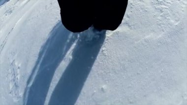 Yakından bakınca, kış mevsiminde dik bir dağ yamacında, derin karların üzerinde yürüyen ayakları görüyoruz.