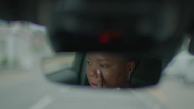 Dikiz aynasında, bir kadın direksiyonun arkasında yansıtılır, ulaşım sırasında odak ve güvenliğin somut bir örneği olarak.