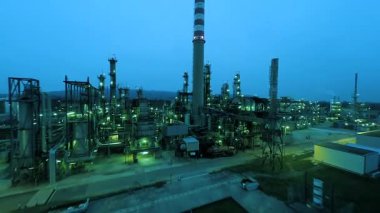 Günbatımında aydınlanan karmaşık bir petrol rafinerisi, tesisin endüstriyel altyapısını ve ekipmanlarını sergiliyor.