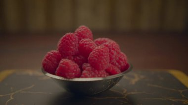 Taze ve olgun ahududu dolu bir kasenin yakından görüntüsü, dokulu ve kırsal bir yüzeye yerleştirilmiş.
