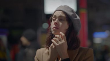 Kahverengi paltolu ve gri bereli bir kadın, elleri bağlı, tren istasyonunda dua ediyor gibi görünüyor..