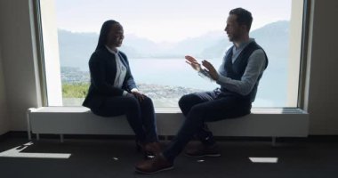 Resimli bir dağ ve göl manzarasına bakan bir ofiste tartışan iki profesyonel.