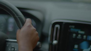 Konsol ve araç içi teknolojiye odaklanmış, direksiyon simidini tutan bir elin yakın çekimi.