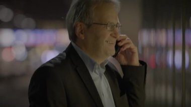 Yetişkin bir iş adamı, gece vakti şehir ortamında telefonla konuşurken ve hayal kırıklığıyla el kol gezerken görülüyor.