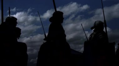 Ortaçağ şövalyeleri ve mızrakları bulutlu bir gökyüzüne karşı antik bir savaş sahnesini andırıyor.