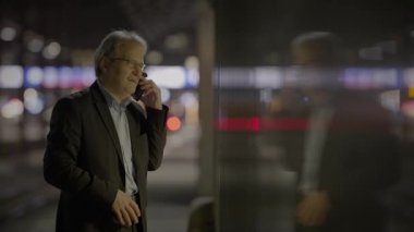 Takım elbiseli bir işadamı, şehir merkezinde geceleri telefonla konuşuyor modern binalar ve aydınlık sokaklarla.
