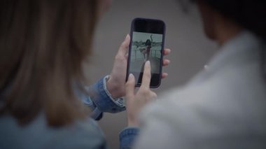 İki arkadaş birlikte akıllı telefon ekranında video izliyorlar, paylaşılan dijital deneyimin tadını çıkarıyorlar.