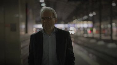 Geceleri, bir işadamı, arka planda bulanık ışıklarla boş bir tren istasyonunda tek başına duruyor.