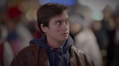 Kapüşonlu ve deri ceketli genç bir adamın portresi, gecenin bir yarısı hareketli bir şehir caddesinde duruyor..