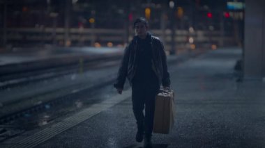 Yalnız bir insan geceleri boş bir tren istasyonunda bavuluyla yürüyor, yalnızlığı ve melankoliyi çağrıştırıyor.