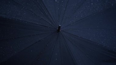 Yağmur damlalarıyla kaplı siyah bir şemsiye yağmurlu bir günün özünü sergiliyor, karamsar ve atmosferik bir görüntü yaratıyor.
