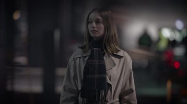 Paltolu ve eşarplı bir kadın bulanık bir şehrin arka planına karşı duruyor.