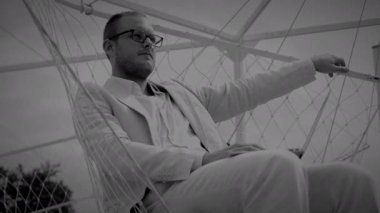 Modern bir açık hava yapısında geometrik çizgiler arasında derin düşüncelere dalmış sakin bir atmosfer yaratan bir adam.