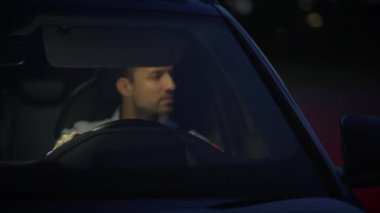 Düşünceli bir adam gece tek başına araba kullanıyor, gösterge paneli ışıklarıyla aydınlatılmış, odaklanmış ve derinlemesine içe dönük.