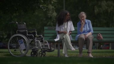 Bakıcı ve yaşlı bir kadın doğayla dolu güzel bir parkta samimi bir konuşma yapıyorlar.