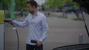 Bir adam, şarj kablosunu uygun bir yerde bulunan bir elektrikli araca dikkatlice bağlar.