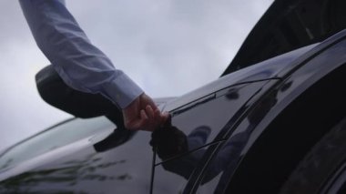 Zarif bir el Halat Bağlantısı kullanarak Kamu Şarj İstasyonunda çalışan elektrikli bir arabanın sapına uzanır. 