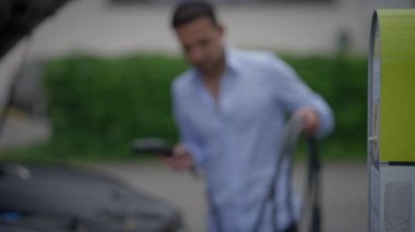 Bir adam elektrik teçhizatını canlı ve yemyeşil şehir ortamında elektrikli bir araca bağlıyor.