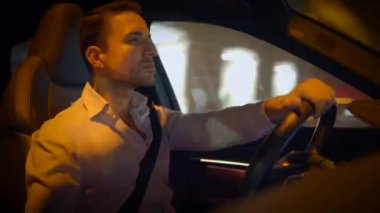 Odaklanmış bir adam, ışıl ışıl sokak lambalarıyla aydınlatılmış canlı bir şehirde ustalıkla araba sürer.