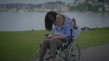 Bakıcı, sakin bir açık hava ortamında yaşlı bir kadınla sevgi dolu bir şekilde iletişim kurar ve şefkat gösterir..